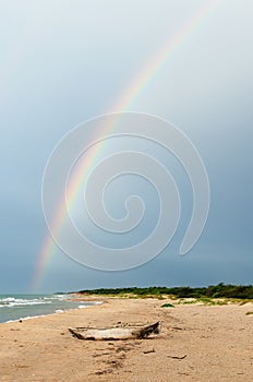 Colombian old dugout canoe on the beach and rainbow