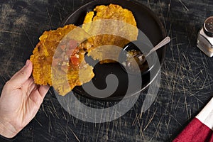 Colombian patacones dish with tomato sauce and onion hogao. Person eating traditional Latin dish. Banished trodden banana photo