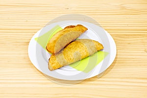 Colombian yellow corn empanadas stuffed with chicken stew with red peppers on white plate and wooden table