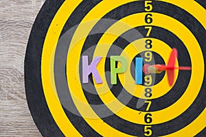 Color alphabets KPI acronym Key Performance Indicator on dartsboard background with red arrow hit center of target.