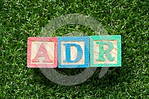 Color block in word ADR Abbreviation of adverse drug reaction on artificial green grass background