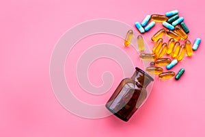 Color blue and yellow pills spilling out of a pill bottle on pink background top view copy space