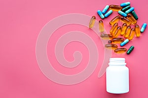 Color blue and yellow pills spilling out of a pill bottle on pink background top view copy space