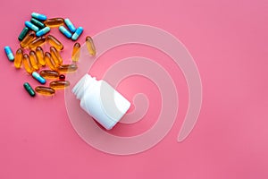Color blue and yellow pills spilling out of a pill bottle on pink background top view copy space
