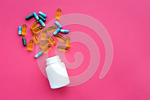 Color blue and yellow pills spilling out of a pill bottle on pink background top view copy space