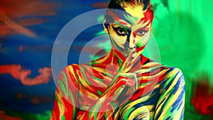 Color face art and body paint on woman holding her finger to her lips in a gesture for silence.. Abstract portrait of