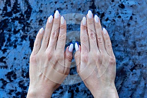 Color French manicure white color with a blue border on the tips of the nails on a velvet blurred background