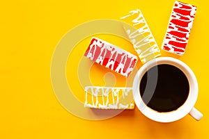 Color glazed cakes and coffee cup on bright yellow background. Top view.