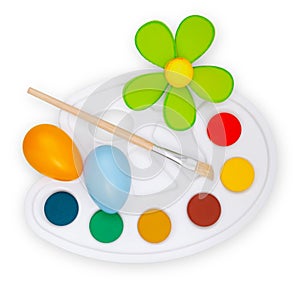 Color palette with paint brushes, flower and colored eggs, top view isolated on a white background. Easter Decorations: Bringing