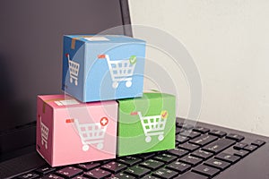 Color parcel carton box with shopping trolley cart printing on laptop computer with white wall background. E-commerce