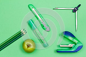 Color pencils, apple, felt-tip pen, paper knife, compass and stapler on green background