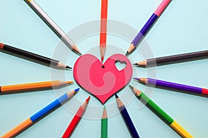 Color pencils in arrange in color wheel colors around wooden red heart on blue background.