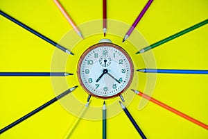 Color pencils and Clock isolated on yellow background.Close up