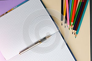 Color pencils lying on pastel purple and beige background near squared notebook. Back to school concept. Colorful art studying and