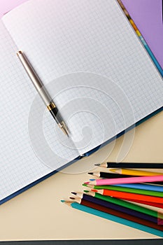 Color pencils lying on pastel purple and beige background near squared notebook. Back to school concept. Colorful art studying and