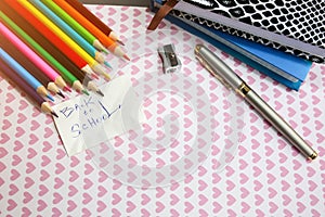 Color pencils, notebooks, sharpener and pen lying on cute background with hearts. Back to school sign written concept. Colorful