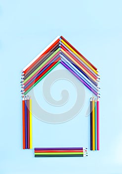 Color pencils in a shape of house on light blue background.