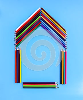 Color pencils in a shape of house on light blue background.
