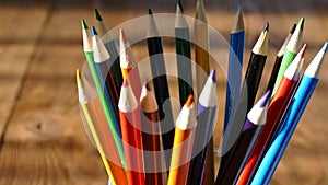 Color pencils in a writing-glass. Draw with colored pencils on white paper and a wooden table. Wooden retro table.