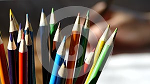 Color pencils in a writing-glass. Draw with colored pencils on white paper and a wooden table. Wooden retro table.