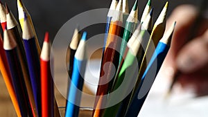 Color pencils in a writing-glass. Draw with colored pencils on white paper and a wooden table. Wooden retro table.