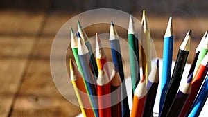 Color pencils in a writing-glass. Draw with colored pencils on white paper and a wooden table. Wooden retro table.