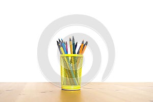 Color pencils in a yellow glass on a wooden table on a white background