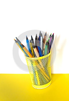 Color pencils in a yellow glass on a yellow table on a white background