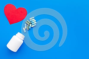 Color pills spilling out of a pill bottle near heart sing on blue background top view copy space