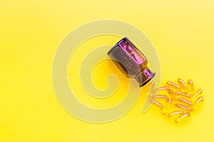 Color pills spilling out of a pill bottle on yellow background top view copy space