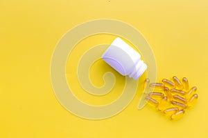 Color pills spilling out of a pill bottle on yellow background top view copy space