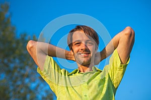 A color portrait photo of a happy smiling brunette haired man wearing a yellow green shirt against a blue sky backround.