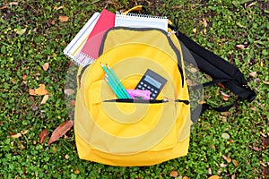 Color rucksack with school stationery on ground outdoors