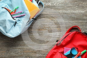 Color rucksacks with school stationery on wooden background