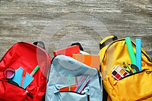 Color rucksacks with school stationery on wooden background