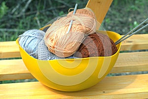 Color skeins of wool yarn, knitting needles and crochet hook in a big yellow bowl