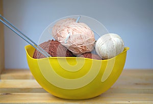 Color skeins of wool yarn, knitting needles and crochet hook in a big yellow bowl