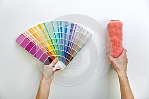 color swatch and paint roller in hands on white wall