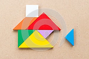 Color tangram that wait triangle piece to complete home shape on wood background Concept about for build dream house,