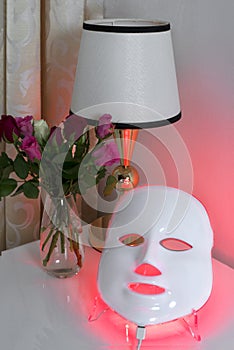 Color therapy mask, vase with roses and a lamp