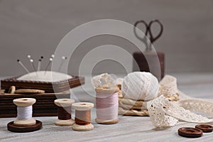 Color threads and different sewing accessories on white wooden table