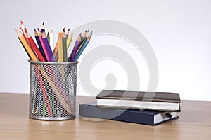 Colore pencils in container standing by notebooks