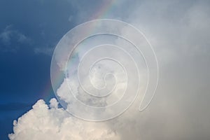 Colored arc of rainbow on the blue sky with white puffy clouds, background
