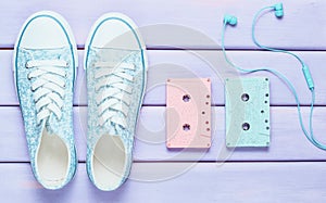 Colored audio cassettes, headphones, sneakers shoes on a purple pastel background. Old-fashioned technologies. Top view. Flat lay.