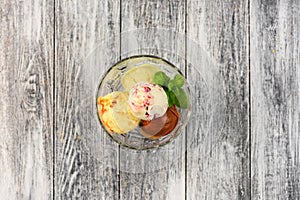 Colored balls of ice cream in a glass cremant on wooden grey background