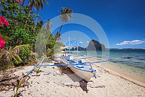 Colored banca boat and vibrant flowers at Las cabanas beach. Surreal landscape in background. Exotic nature scenery in El Nido,
