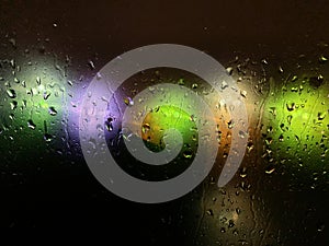 Colored blurry lights on a dark background through the drops on the glass