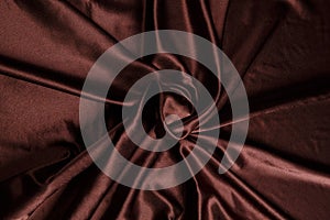 Colored brown textile satin fabric folded in folds and waves with highlights and texture