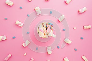 Colored candies and marshmallow with cappuccino mug on pink background. Flat lay, top view. Rainbow sugar cane in mug with coffee