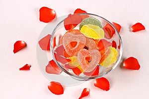 Colored candies with two red hearts in glass bowl and rose petals